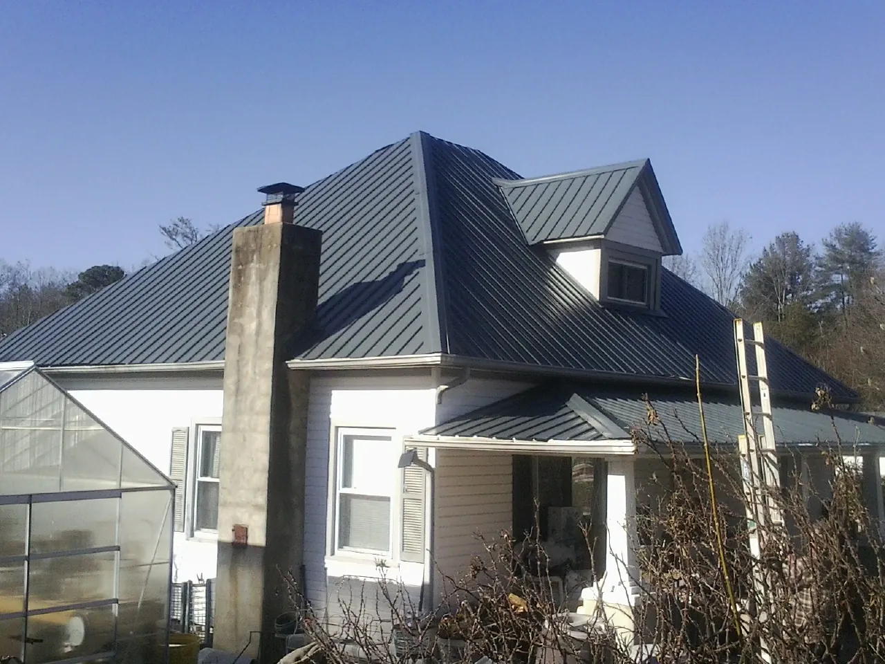 Dark blue standing seam metal roof on a white farmhouse with dormer — Slate & Tile Roof Repair by Roofing Brothers in Jean