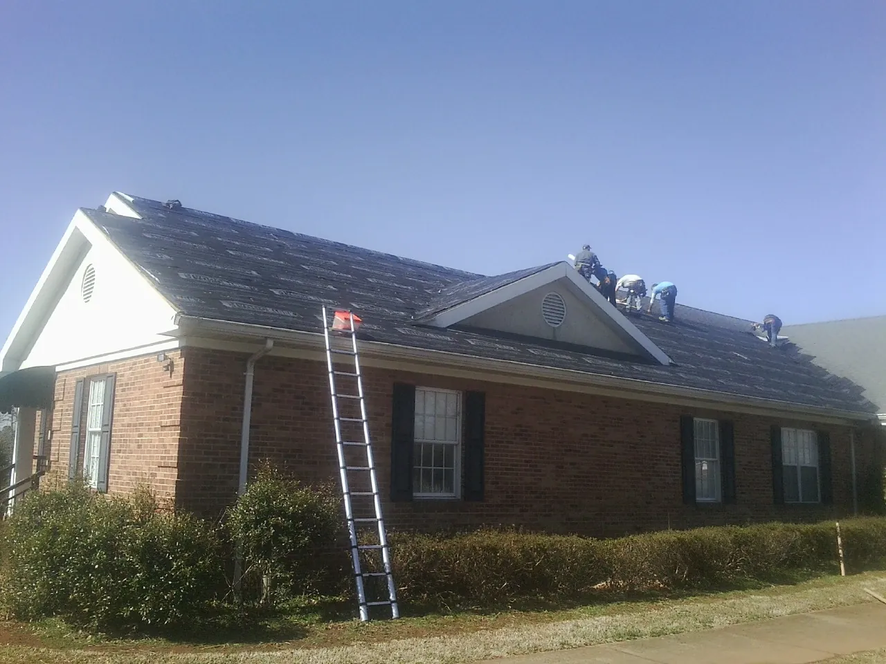 Crew tearing shingles off a brick ranch roof with a ladder set — Emergency Roof Repair work by our crew in Jean