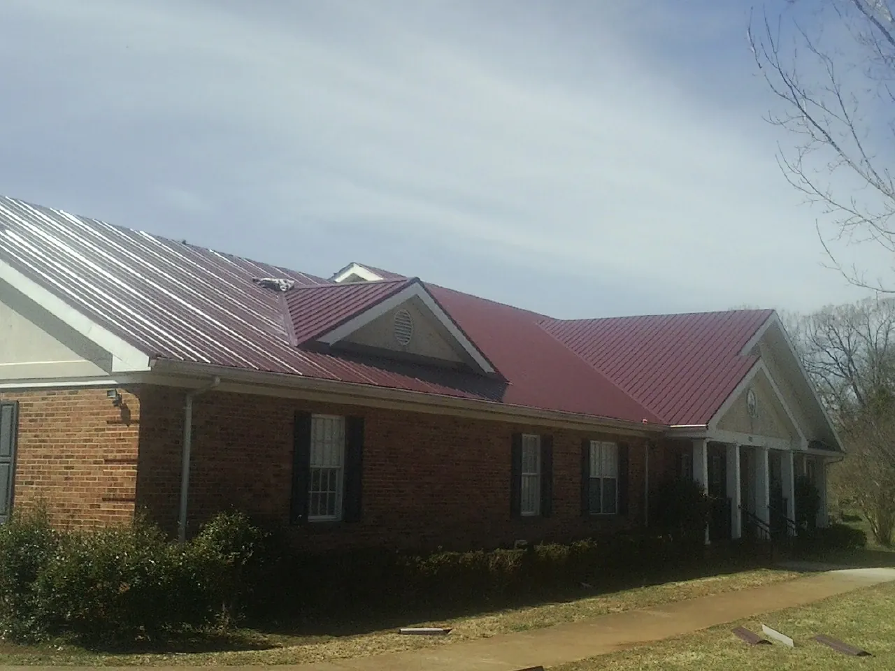 Red metal roof with gabled entries on a long brick building, from a Hail Damage Roof Repair job in Jean