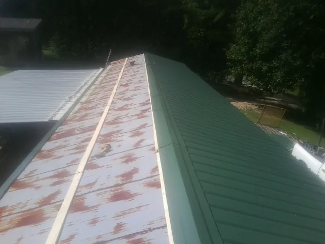 Old rusted panels beside newly installed green metal roofing — Wind Damage Roof Repair by Roofing Brothers in Jean
