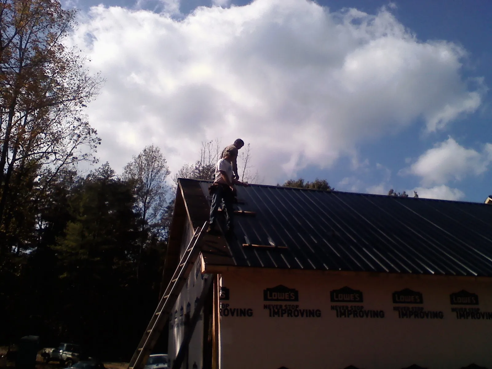 Roofer fastening dark metal panels high against a cloudy sky, from a Roof Inspection job in Jean