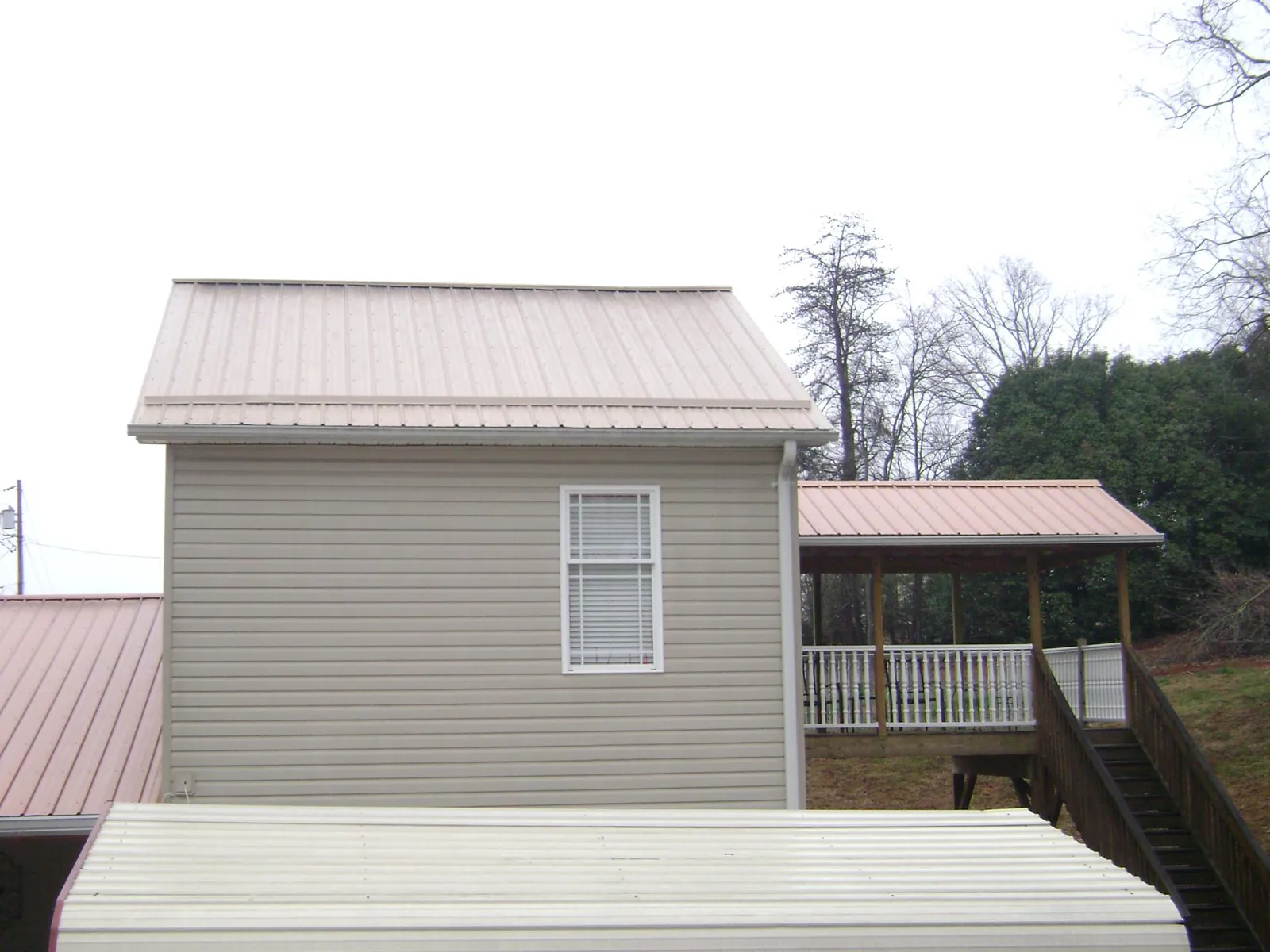 Tan metal roofs on a two story addition and attached porch, from a Roof Replacement job in Jean